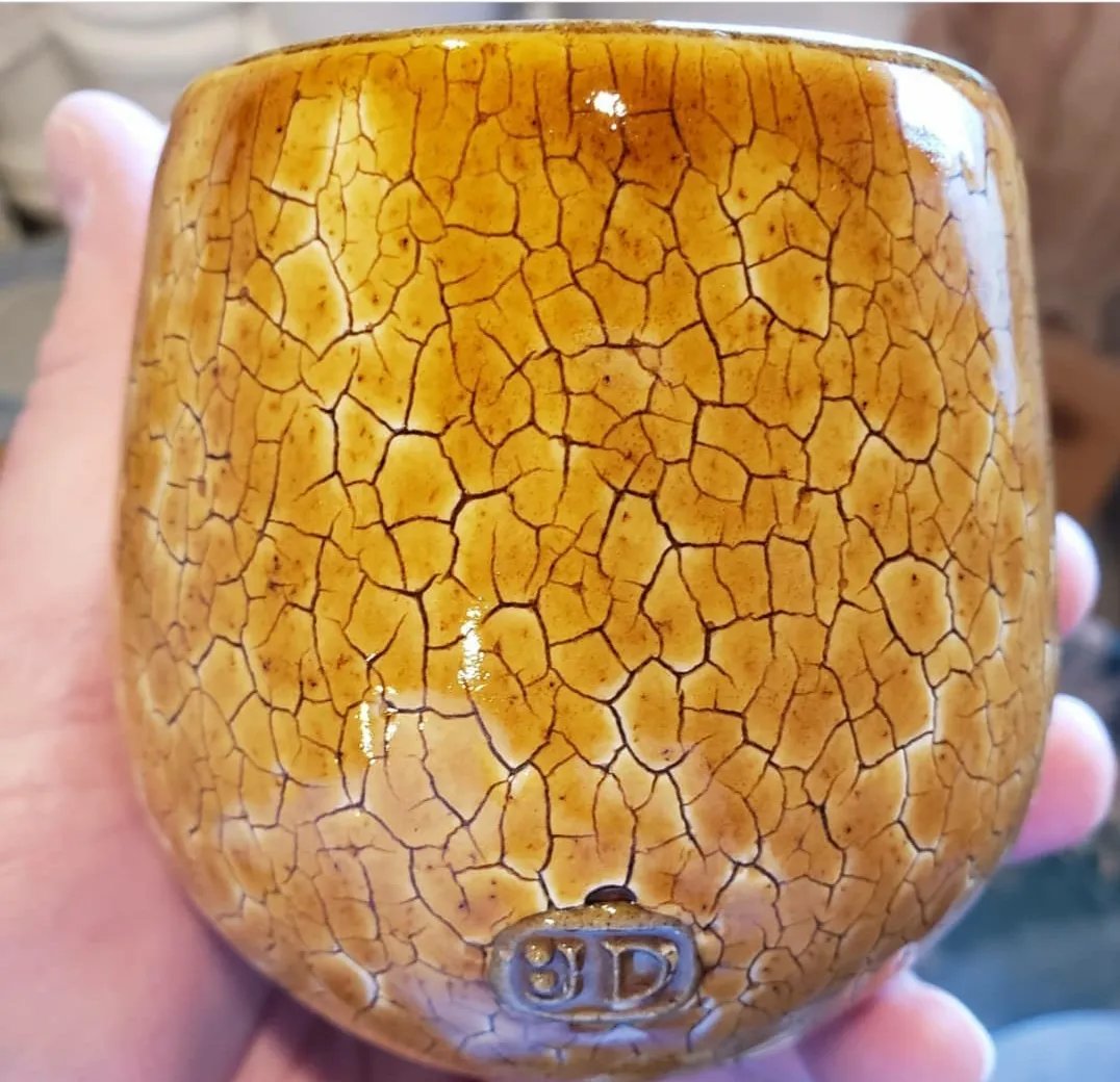 A pottery mug with a honey over-glaze that highlights an engobe having a decorative crack pattern