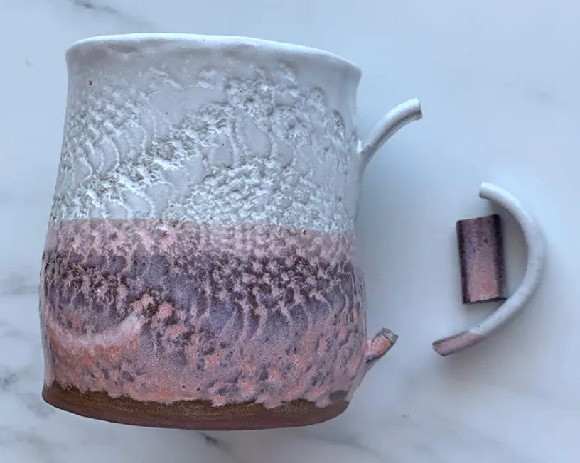 The handle on a pottery mug has cracked in two places.